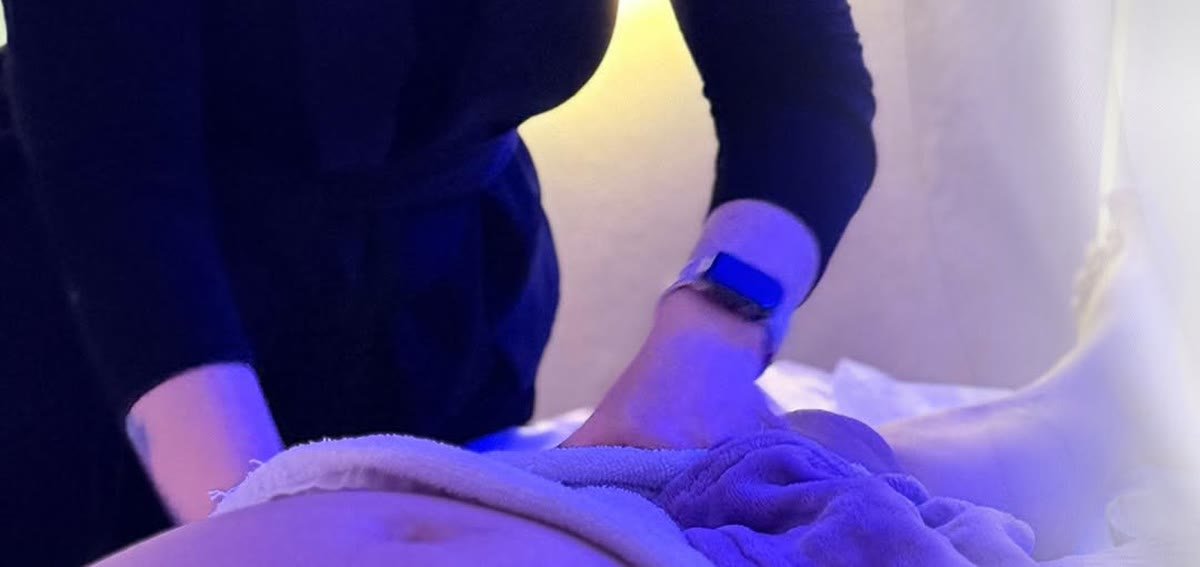 Mãos da profissional fazendo drenagem na barriga de uma gestante, sob luz suave