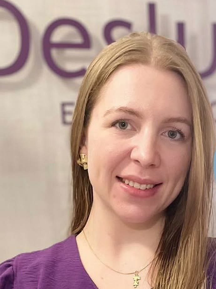 Profissional da Deslum Estética sorrindo na recepção, em frente ao painel com o logo da clínica