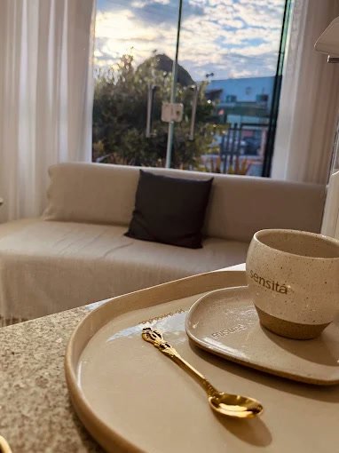 Sala de espera da Sensitá Clinic, com sofá claro, luz de fim de tarde e uma xícara da casa sobre a mesa